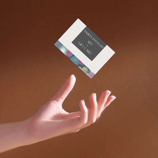Hand reaching out towards a gift card with 'Ashley Hannah Art' on a brown background
